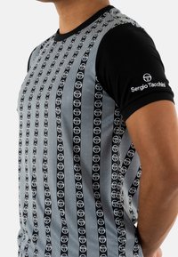 Camiseta de manga corta negra y gris con rayas verticales y un patrón de logo repetido. Presenta mangas negras y cuello redondo.