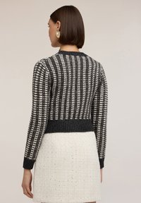 Suéter corto a rayas grises y blancas con dobladillo y puños acanalados, con una textura de punto. Usado sobre una falda texturizada de color claro.