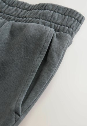 Detailní záběr na kapsu šedých tepláků a elastický pas na světlem pozadí.