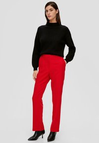 Czarny sweter prążkowany z wysokim kołnierzem, zestawiony z czerwonymi dopasowanymi spodniami i czarnymi, eleganckimi botkami na obcasie. Prosty design z czystymi liniami.