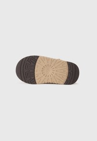 Semelle de chaussure avec une section en caoutchouc noir présentant un motif de texture et une semelle intermédiaire contrastante beige clair avec des motifs géométriques.