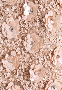 Primo piano di un tessuto in paillettes beige decorato con paillettes a forma di fiore sovrapposte, ciascuna centrata da un piccolo strass trasparente.