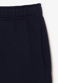 Pantalon de survêtement bleu marine avec ceinture élastique et poche latérale, montrant la partie supérieure des hanches et de la taille sur fond blanc.