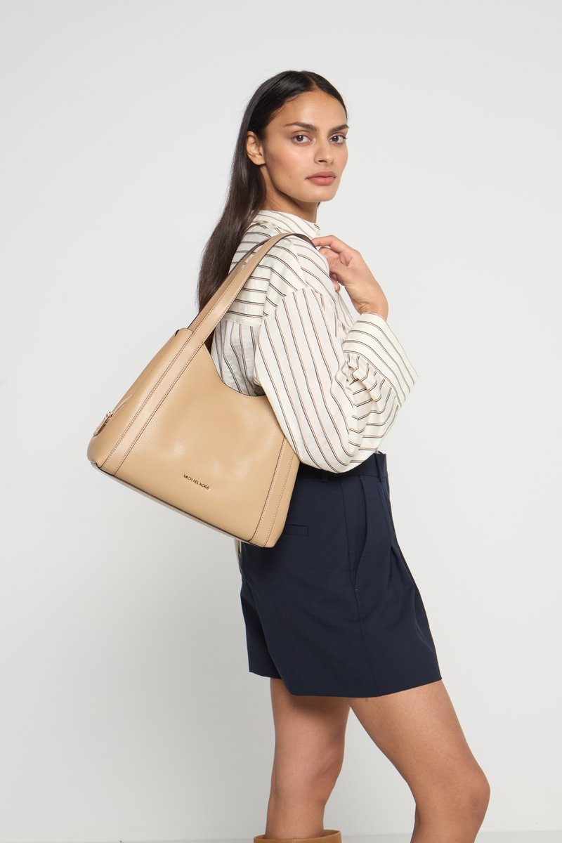 Bolso hobo de cuero marrón claro con una textura suave y un logo sutil. Presenta una silueta curva y una larga correa para el hombro que facilita su transporte.