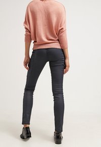 Pullover oversize rosa chiaro e pantaloni aderenti grigi scuri, con una texture liscia e un design elegante. Le scarpe nere completano l'outfit.