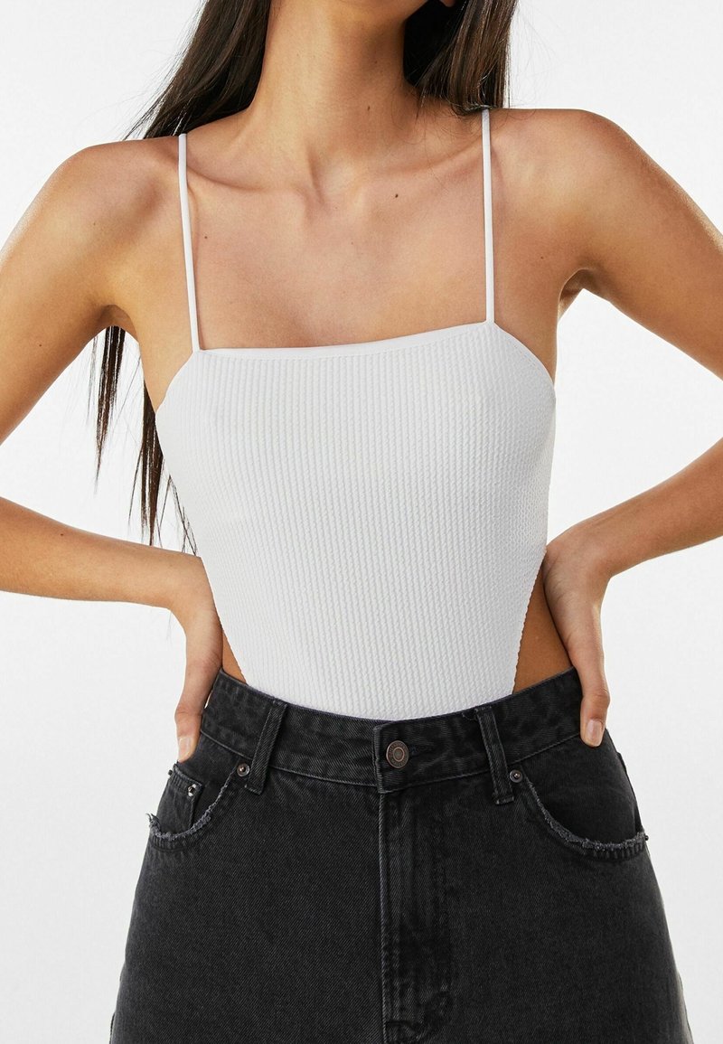 Vit ribbad bodysuit med tunna axelband, med en fyrkantig halsringning och en figurnära design, kombinerad med högmidjade svarta denimshorts.