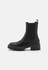Bottines chelsea noires en cuir lisse avec panneaux élastiques latéraux, semelle épaisse et une languette pour un enfilage facile. Intérieur doublé d'un matériau doux.