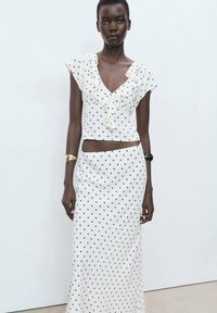 White polka-dot crop top with ruffled neckline paired with a long polka-dot skirt. Smooth fabric, fitted design, minimalistic color scheme.
