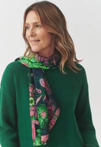 Écharpe en soie multicolore arborant des motifs verts, roses et marins avec des designs floraux et à pois, drapée élégamment autour du cou.