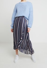Light blue knitted sweater, long dark blue skirt with vertical stripes in pink and white, featuring a ruffled hem, paired with white sneakers.