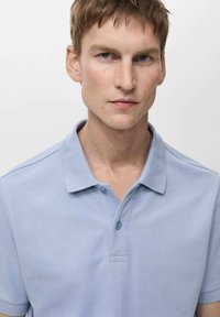 Vaaleansininen polo-paita puuvillasekoitekankaasta, jossa on klassinen kaulus, kolmen napin lista ja lyhyet hihat, joissa on tekstuuri.