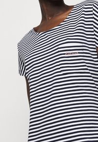 Koszulka w paski z poziomymi niebieskimi i białymi paskami, okrągłym dekoltem, krótkimi rękawami oraz małą kieszonką na piersi z haftowanym detalem.