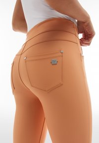 Pantaloni skinny-fit color pesca, realizzati in un materiale liscio e stretch. Presentano una vita alta, tasche posteriori e dettagli in metallo argentato.