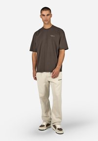 Camiseta de algodón marrón con mangas cortas y cuello redondo. Combinada con pantalones deportivos beige claro con un pequeño logo negro.