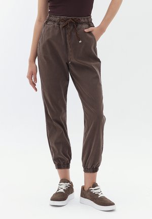 Pantaloni jogger marroni con vita elasticizzata, cordoncino e caviglie con polsini, realizzati in un tessuto morbido. Abbinati a sneaker marroni scuri.