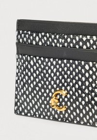 Μαύρη και λευκή υφασμάτινη θήκη καρτών με χρυσό διασυνδεδεμένο λογότυπο CC στην κάτω δεξιά γωνία, με λείο μαύρο δερμάτινο φινίρισμα.