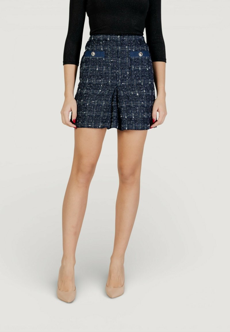 Námořnicky modré tweedové šortky s texturovaným vzorem, vybavené dvěma předními kapsami, stříbrnými knoflíky a přiléhavým pasem, doplněné tělovými vysokými podpatky.