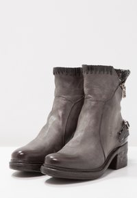 Schwarze Leder-Ankelstiefel mit abgerundeter Zehe, dekorativen Nähten und einem strukturierten Akzent am Schaft. Mit einem seitlichen Reißverschluss und einer kleinen Schnalle.