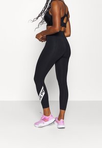 Czarne legginsy sportowe z wysokim stanem, z białym logo "KEEP" z boku, w połączeniu z różowymi butami sportowymi i czarnym stanikiem sportowym.