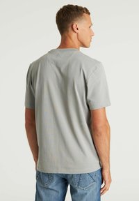 Siva pamučna majica s kratkim rukavima, suptilnom teksturom i trokutastim šavom na leđima, u kombinaciji s plavim trapericama.