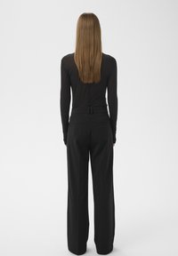 Schwarzes langärmliges Oberteil mit figurbetontem Schnitt, kombiniert mit weit geschnittenen schwarzen Hosen, die einen gebundenen Taillenbund und dezente Taschen auf der Rückseite haben.