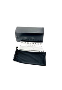 Černá krabička Oakley s logem, uvnitř se nachází tištěný manuál a měkký černý sáček na stahovací šňůrku. Obal má elegantní design.