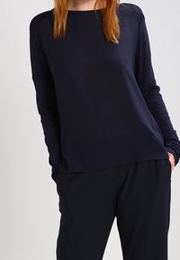 Haut à manches longues bleu marine en tissu lisse, doté d'un col rond simple et d'une coupe décontractée. Associé à un pantalon noir ample.