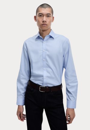 Hellblaues Hemd mit langen Ärmeln, aus Baumwolle. Kombiniert mit dunklen Jeans und einem braunen Gürtel. Einfaches Kragenmuster.
