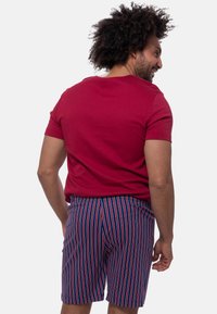 Rød t-shirt med korte ærmer; blå shorts med lodrette røde og hvide striber; afslappet pasform; materialet er bomuldsagtigt, glat tekstur.