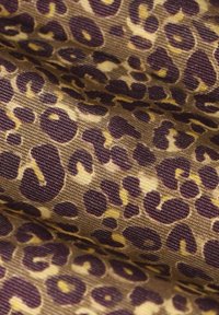 Tissu à imprimé léopard présentant des taches contrastées en violet foncé et jaune sur un fond fauve, avec une apparence texturée et tissée.