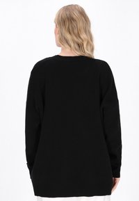 Pulover negru din tricot cu un croi lejer, având mâneci lungi, decolteu rotund și cusături vizibile pe spate. Textură moale.
