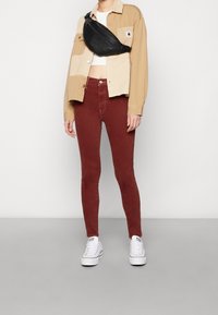 Jeans ajustados color marrón, chaqueta beige con diseño de patchwork, top corto blanco y un bolso de cintura negro. Las zapatillas son de lona blanca con cordones.