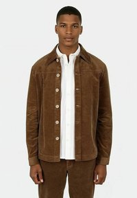 Bruin corduroy jasje met een kraag, voorknoopsluiting en textielstof. Draag het over een wit overhemd met knopen. Effen achtergrond.