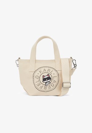 Μικρή μπεζ τσάντα από καμβά με διπλές λαβές, αποσπώμενο φαρδύ ιμάντα ώμου και μαύρο κυκλικό λογότυπο με πουά που απεικονίζει μια γάτα με γυαλιά ηλίου.