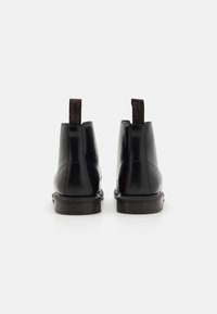 Botines de cuero negro con acabado suave, suelas texturizadas y dos tiradores en la parte trasera que presentan un texto rojo en contraste.