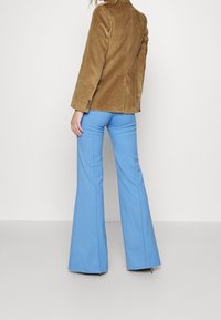 Brun corduroy blazer med lodrette striber og knapdetalje, parret med blå klokkeformede bukser med en glat tekstur.