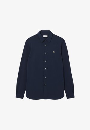 Temno modra srajca z gumbi iz bombaža z dolgimi rokavi in pointed ovratnikom. Ima majhno zeleno logo na levi prsni strani.