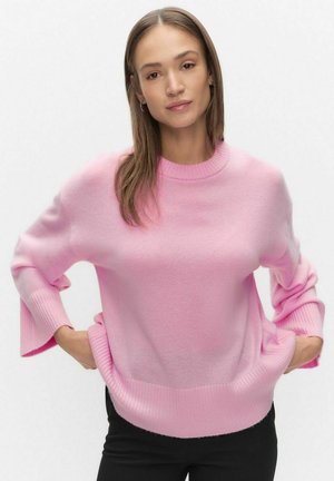 Rosa tröja med mjuk textur, rund halsringning och vida ärmar. Ribbstickade muddar och fåll. Kombinerad med svarta byxor.