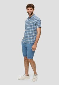 Blauwe geruite korte mouwen shirt gecombineerd met lichtblauwe opgerolde shorts en witte sneakers. Beschikt over een knoopsluiting aan de voorkant en een klassieke kraag.