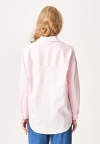 Lyserød langærmet skjorte med klassisk krave og knapmanchetter, med en lige rygstropp og en buet kant, båret med blå jeans.