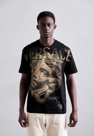 T-shirt en coton noir avec un grand motif doré représentant un visage classique, avec le texte "VERSACE" au-dessus et "SINCE 78" en dessous en blanc.