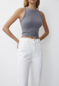 Gray ribbed tank top with a high neckline, paired with high-waisted white jeans, showcasing a fitted design and smooth texture.