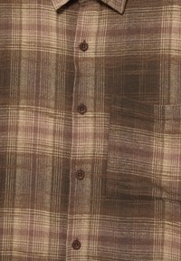 Rjava in bež srajca s karo vzorcem in dolgimi rokavi, z ovratnikom in štirimi rjavimi gumbi. Vključuje prsni žep.