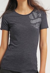 Camiseta gris de manga corta hecha de tela suave, que presenta un diseño gráfico con lunares blancos y texto en la parte superior izquierda.