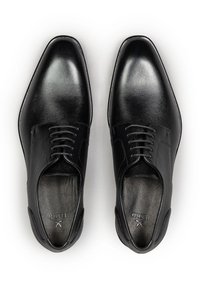 Een paar zwarte gepoetste leren nette schoenen met veters, gezien van bovenaf op een witte achtergrond.