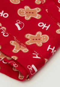 Červená tkanina s opakujícími se vzory perníčků a Santa klobouků, s bílým textem "HO". Měkčí textura a viditelné standardní šití.