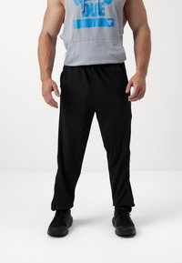 Calças atléticas pretas feitas de um tecido leve com um corte descontraído. Características notáveis incluem zíperes laterais e um cós elástico.