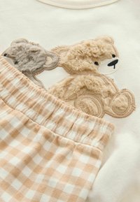 Helles Sweatshirt mit plüschiger Teddybär-Stickerei in Beige und Braun, kombiniert mit karierter beiger und weißer Schlafshorts.