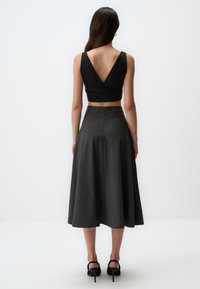 Zwarte crop top met wikkelmodel en V-hals, gecombineerd met een grijze, knielange A-lijn rok met een gladde textuur en een verborgen rits aan de achterkant.