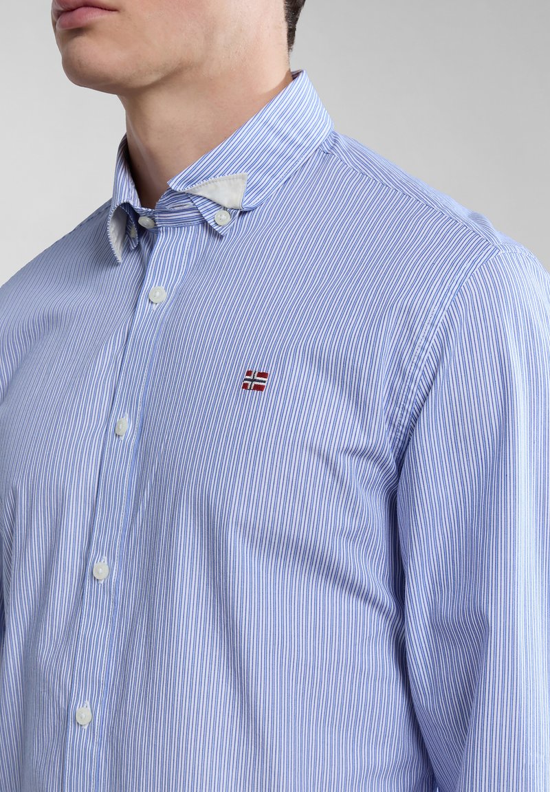 Koszula zapinana na guziki wykonana z materiału w niebieskie i białe paski. Posiada kontrastowy biały kołnierzyk oraz małe haftowane logo na piersi.